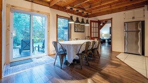 A dining area with a wooden ceiling, a large table with chairs, and a view through glass doors to an outdoor deck. - Au Chic Chalet des Chutes | Chic Chalet | Spa (Sainte-Mélanie)