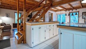 A spacious kitchen with white cabinets, a wooden staircase, and a large island with a sink. - Au Chic Chalet des Chutes | Chic Chalet | Spa (Sainte-Mélanie)