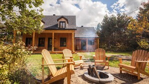 A wooden cabin with a porch, outdoor seating, and a fire pit. - Au Chic Chalet des Chutes | Chic Chalet | Spa (Sainte-Mélanie)