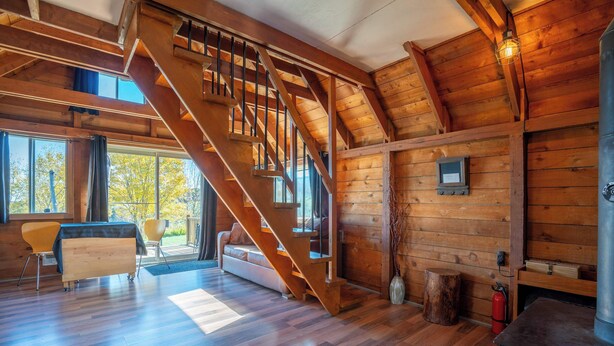 Una habitación espaciosa con una escalera de madera, una chimenea y un ventanal con vistas al exterior.