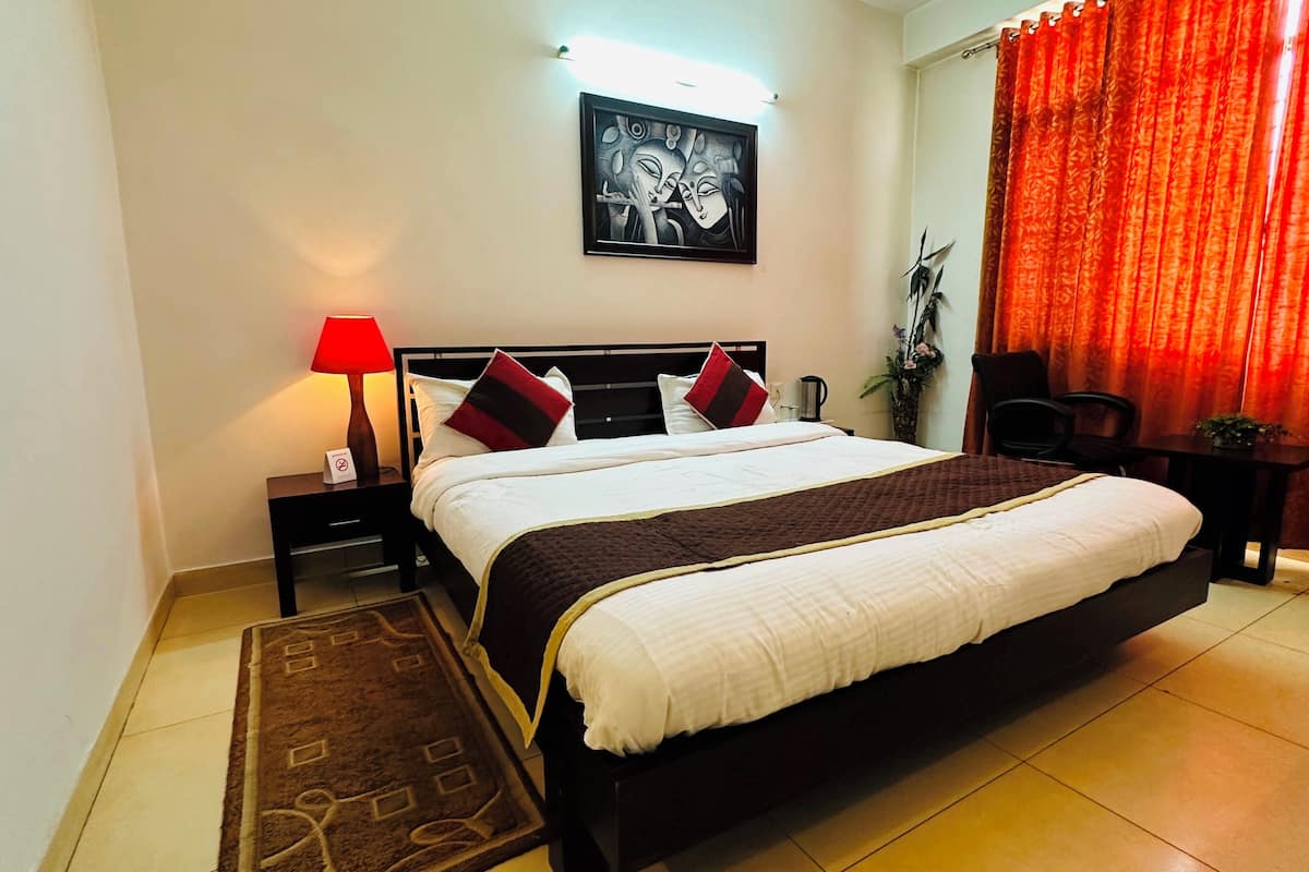 Een hotelkamer met een groot bed, een nachtkastje met een lamp, een lijst met een afbeelding aan de muur en een rood gordijn.