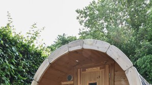 A wooden barrel-shaped structure with a door, a small table, and a bench.