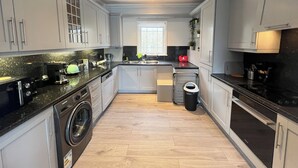 A modern kitchen with grey cabinets, a washing machine, a dishwasher, and a stove. - 3 Bedroom House in London - Private Garage - Wi-fi (Croydon)