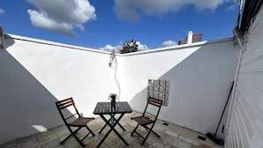 A small patio with two wooden chairs and a table, a tiled floor, and a white wall. - 3 Bedroom House in London - Private Garage - Wi-fi (Croydon)