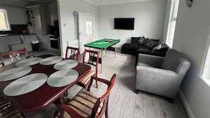 A modern living room with a pool table, a grey sofa, and a dining area with a wooden table and chairs. - 3 Bedroom House in London - Private Garage - Wi-fi (Croydon)