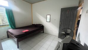Um quarto pequeno e modesto, com uma cama, um ventilador e uma porta.