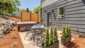 A patio with a hot tub, metal chairs, and two potted plants.