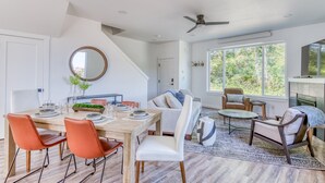 A modern living room with a dining area, large windows, and a ceiling fan. - Harbor Lights 540 (#2) | Private Hot Tub, Harbor Walks & Family Time (Depoe Bay)