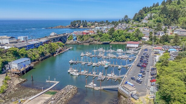 An aerial view of a marina with boats docked, a bridge, and surrounding residential buildings. - Harbor Lights 540 (#2) | Private Hot Tub, Harbor Walks & Family Time (Depoe Bay)