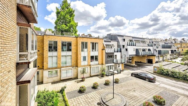 Ein modernes Wohngebäude mit mehreren Etagen, großen Fenstern und einem gepflasterten Innenhof mit Kübelpflanzen.