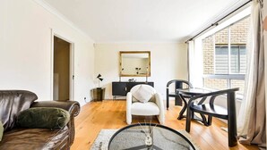 Ein Wohnzimmer mit einem Ledersofa, einem weißen Sessel, einem runden Glastisch und einem Essbereich mit Tisch und Stühlen.