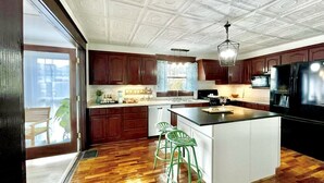 Una cocina con armarios de madera, una isla central, taburetes de bar verdes y un refrigerador grande.