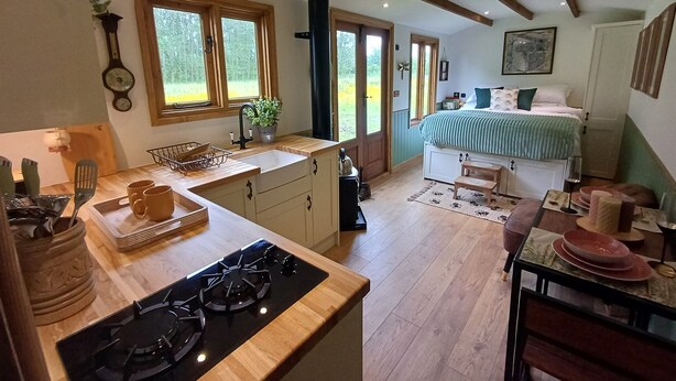A kitchen with wooden countertops, a stove, and a sink. There is a dining area with a table and chairs. - The Botanist - Luxury Cabin With Hot Tub Near York (York)