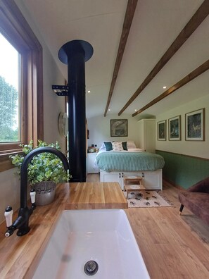 A bedroom with a bed, bedside tables, a window, a black column, and a sink. - The Botanist - Luxury Cabin With Hot Tub Near York (York)