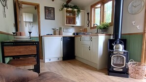 A cozy kitchen with wooden beams, a black stove, and a dining area with a brown chair. - The Botanist - Luxury Cabin With Hot Tub Near York (York)
