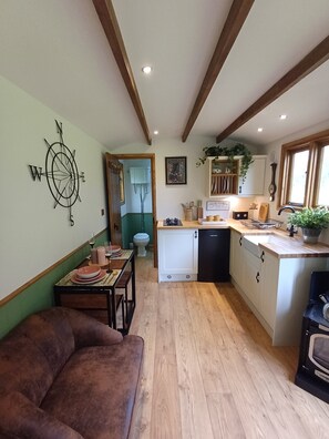 A compact kitchen with wooden beams, a dining area with a brown sofa, and a visible toilet. - The Botanist - Luxury Cabin With Hot Tub Near York (York)