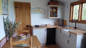A kitchen with wooden cabinets, a built-in dishwasher, a wooden dining table with chairs, and a sign indicating 'LEMONADE SOLD HERE'.