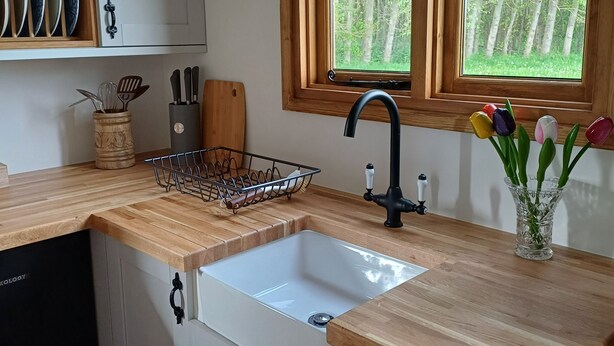 A kitchen with a wooden countertop, a sink, and a window with a view of trees.