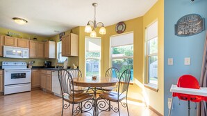 A kitchen with wooden cabinets, a white stove, a dining table with four chairs, and a red high chair.