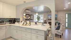 Una cocina moderna con armarios gris claro, una isla grande con un fregadero y una zona de comedor con una silla azul.