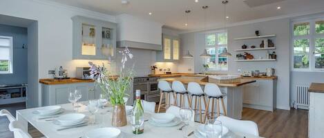 A modern kitchen with white cabinetry, a central island with bar stools, and a dining area set for six.