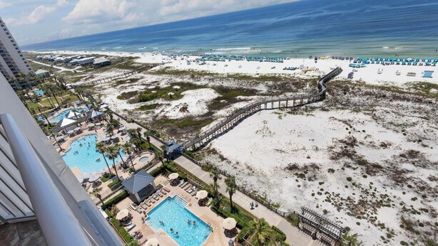 Un complejo turístico con varias piscinas, una zona de playa con sombrillas y un paseo marítimo que conduce a la playa.