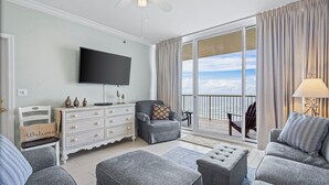 Una sala moderna con televisor de pantalla plana, sofás grises, un aparador blanco y un balcón con vistas.