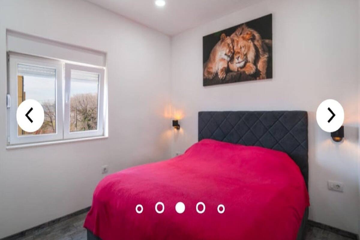 Une chambre à coucher avec un lit, une fenêtre, un tableau représentant des lions et des lampes fixées au mur.