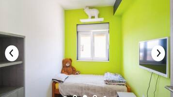 A small, bright room with a bed, a teddy bear, a window, and a TV.
