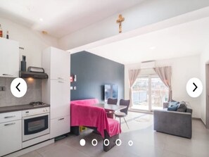 Una cocina moderna con armarios blancos, estufa a gas y un comedor con mantel rosa.
