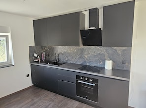 A modern kitchen with dark cabinetry, a marble backsplash, and built-in appliances. - Apartments Andrea (Split)
