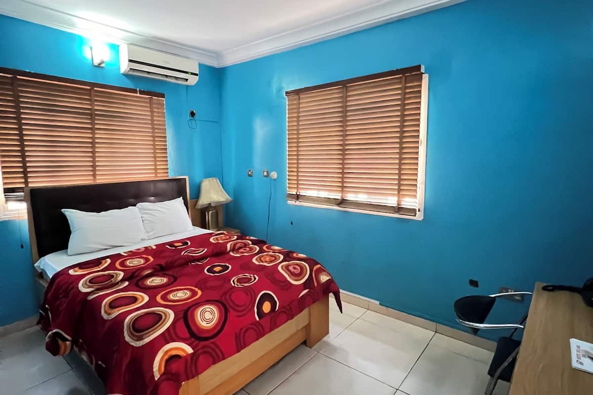 A bedroom with a bed, a desk, and two windows with blinds.