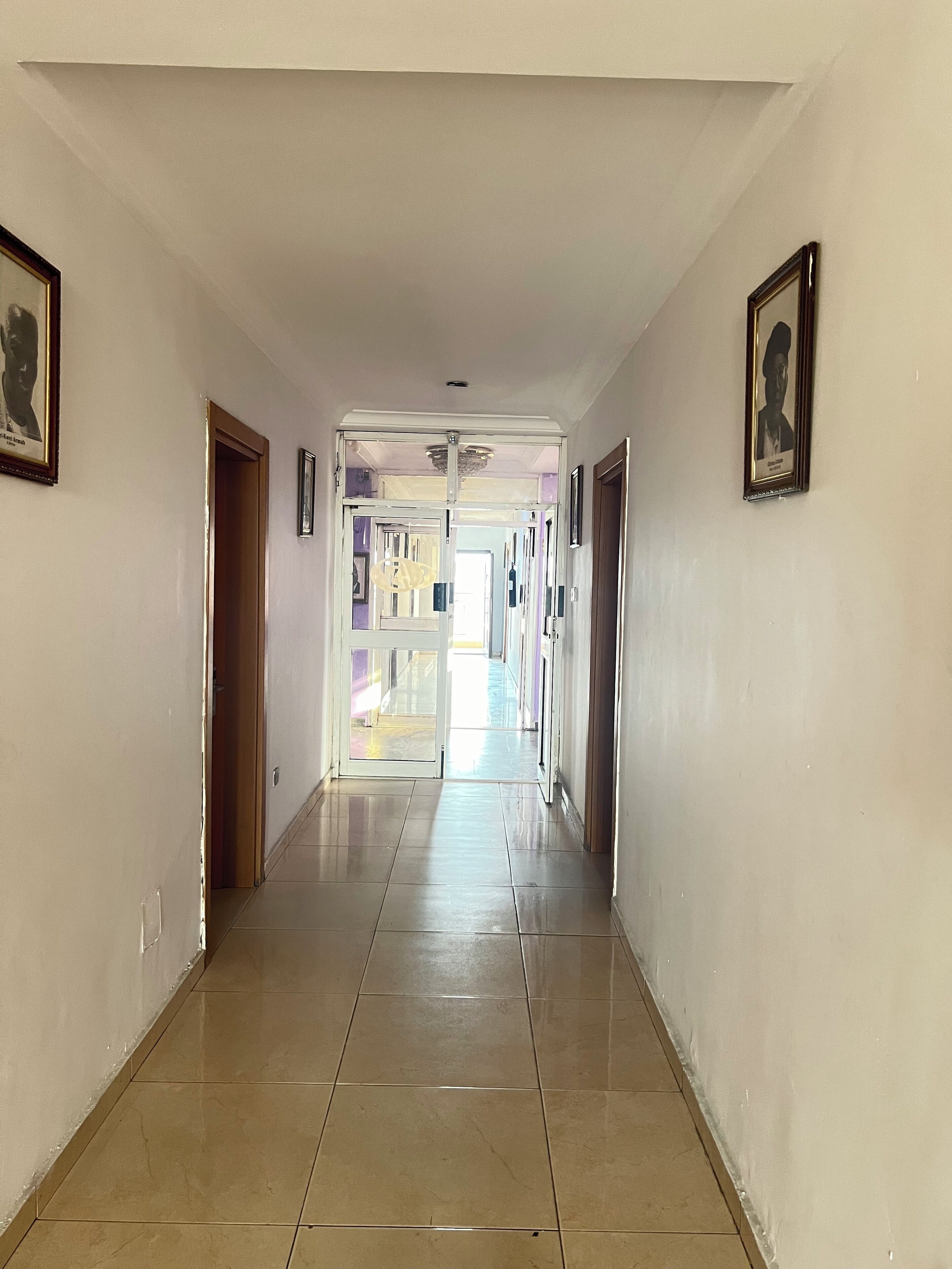 A hallway with tiled flooring, doors on both sides, and framed pictures on the walls.