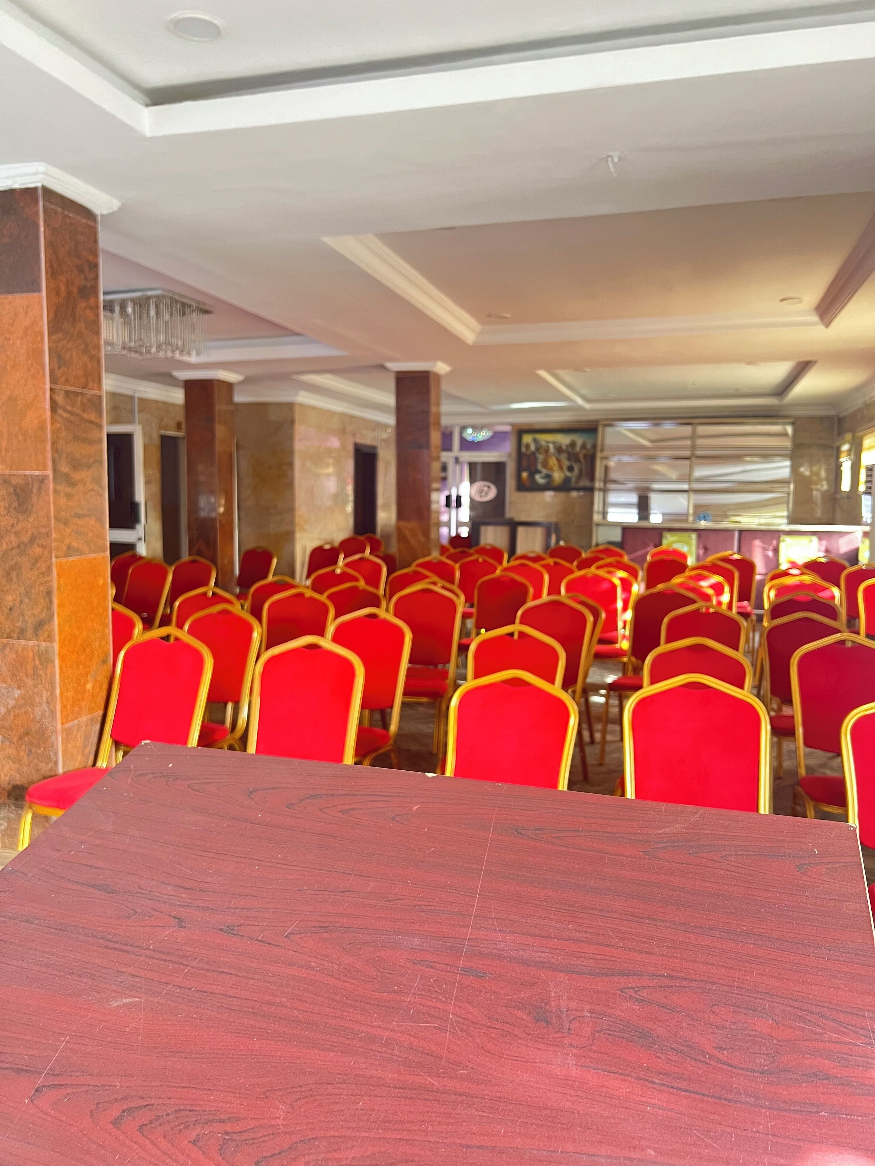 A banquet hall with rows of red chairs and a large wooden table in the foreground.