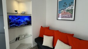 Ett vardagsrum med en väggmonterad TV, en inramad tavla och en röd soffa.