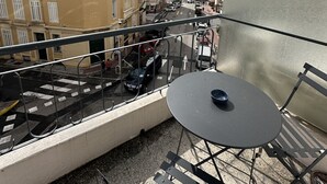 En balkong med ett bord och stolar, med utsikt över en gata med parkerade bilar och byggnader.