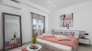 A modern bedroom with a large mirror, a bed with pink bedding, a small round table with a plant, and a painting on the wall. - Villa Lemily (Matulji)