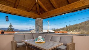 A covered outdoor seating area with wicker furniture, a table, and a stone pillar. - Villa Lemily (Matulji)