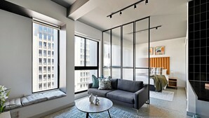 Een moderne woonkamer met een grijze bank, een ronde salontafel en een groot raam met uitzicht op de stad.
