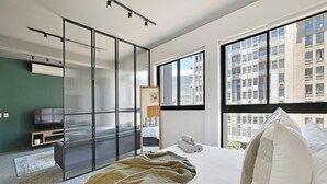 Een moderne hotelkamer met een groot bed, een televisie, een schuifdeur en uitzicht op de stad.