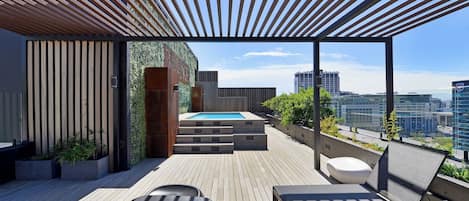 A rooftop terrace with a pool, seating, and a view of the city.