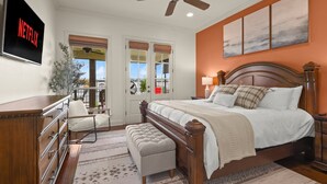 A bedroom with a wooden bed, a ceiling fan, a TV mounted on the wall, and a large window with a view of the outside. - False River Waterfront - Pets - Fire Pit - Porch (Ventress)