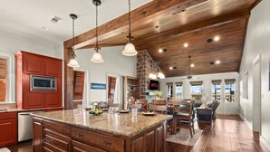 A spacious kitchen with a large island, wooden ceiling beams, and a stone fireplace. - False River Waterfront - Pets - Fire Pit - Porch (Ventress)