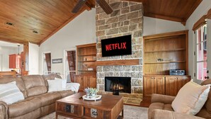 A cozy living room with a stone fireplace, leather sofas, wooden shelves, and a Netflix sign. - False River Waterfront - Pets - Fire Pit - Porch (Ventress)