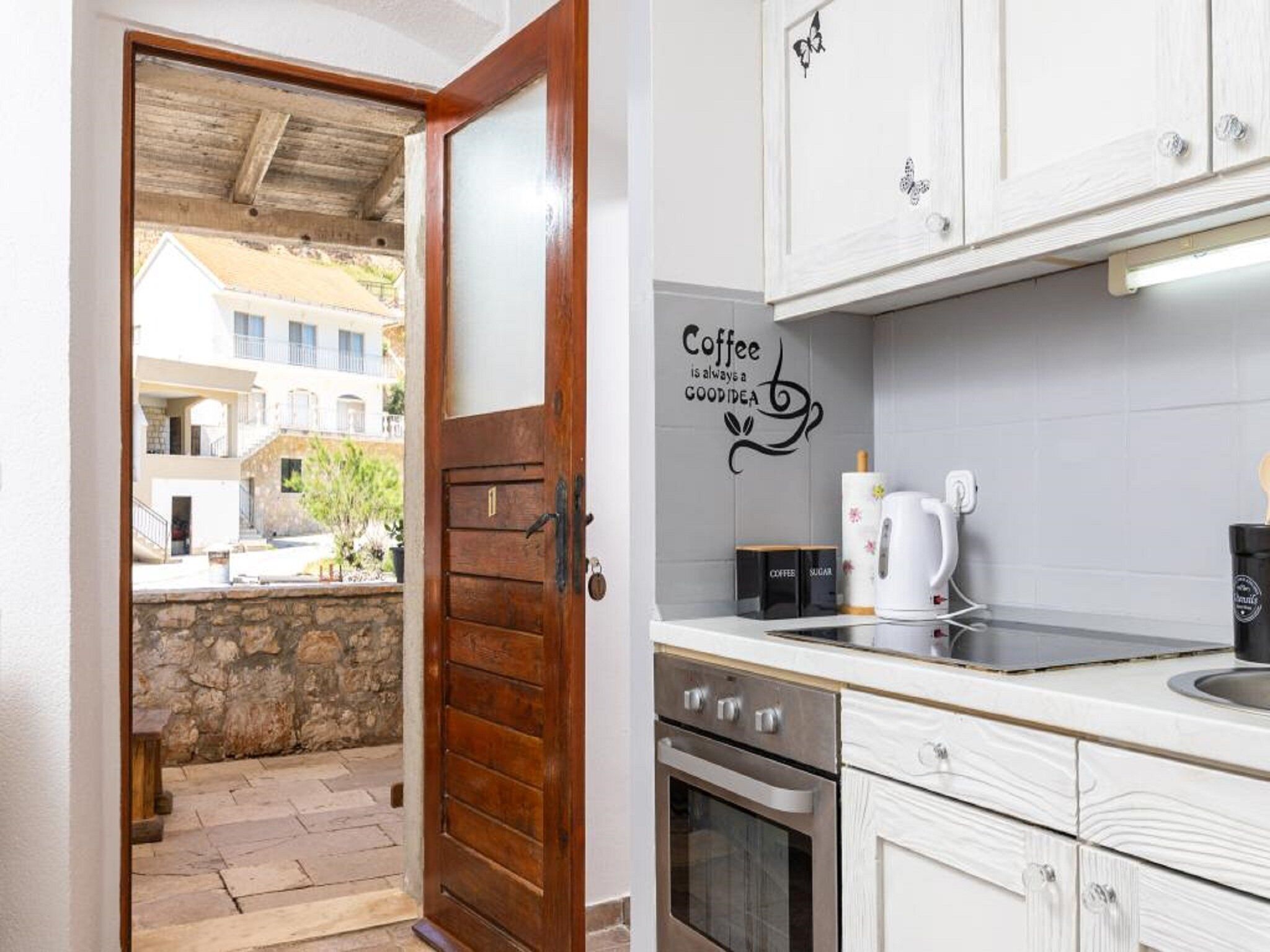Une cuisine avec un motif décoratif sur le mur représentant des thèmes liés au café, une machine à café et une vue sur un mur de pierre et des bâtiments à l’extérieur.