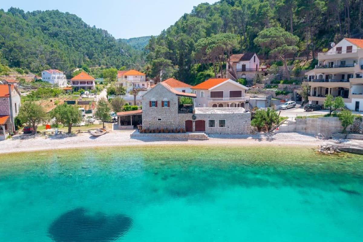 Un pueblo costero con edificios de piedra, un mar turquesa cristalino y una formación rocosa con forma de corazón.