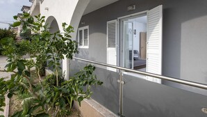 Een balkon met een metalen hekwerk, een bloempot en een raam met witte luiken.