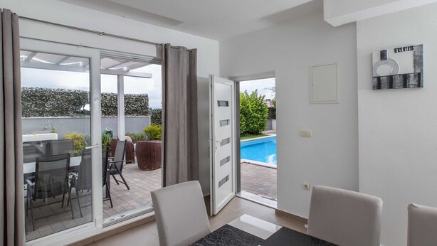 Een moderne woonkamer met een glazen deur die leidt naar een balkon met buitenmeubilair en een zwembad.