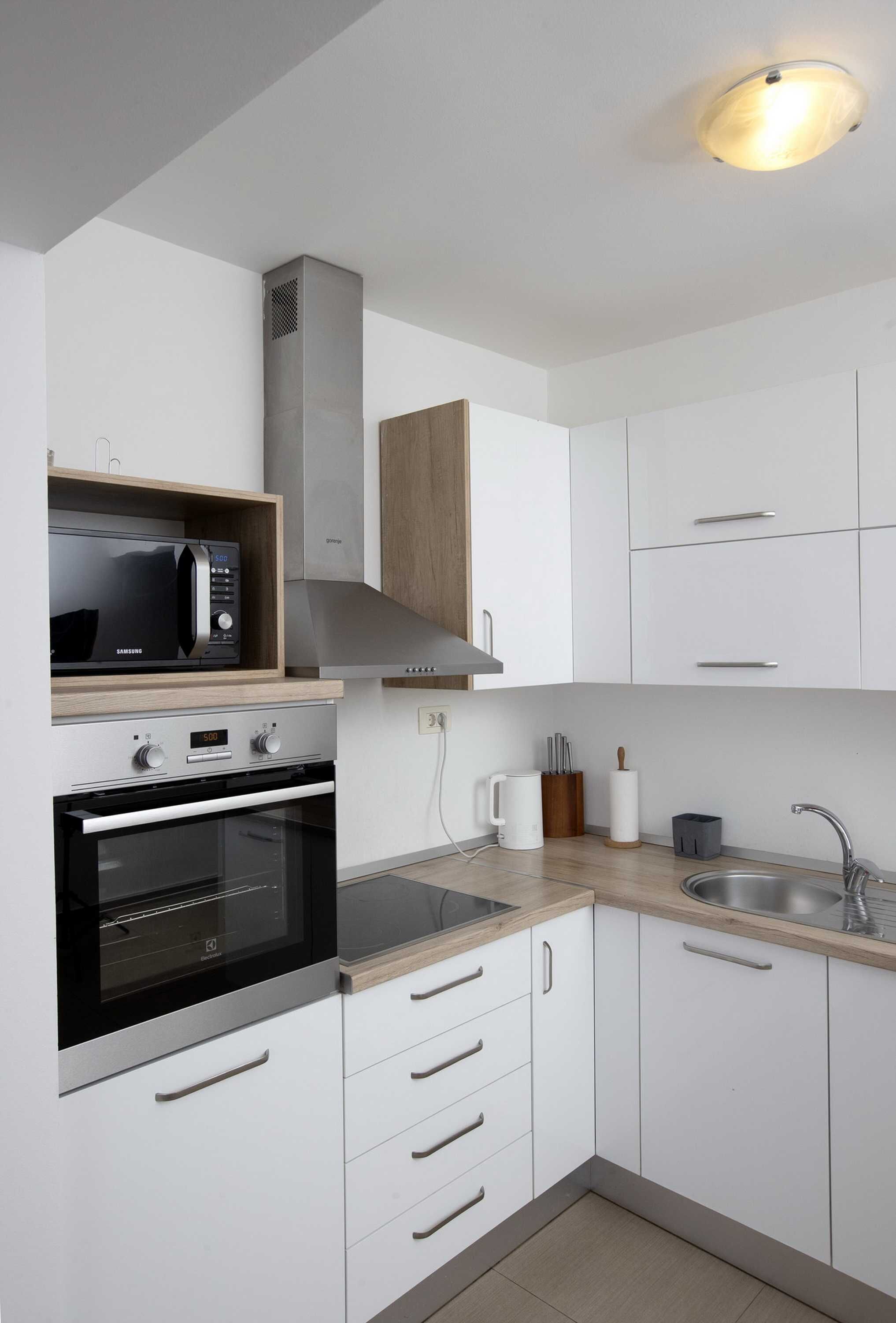 A modern kitchen with white cabinets, a built-in microwave, an oven, and a stainless steel sink.