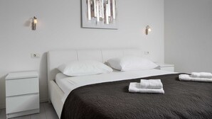 Een moderne slaapkamer met een wit bed, een donker dekbed, twee witte kussens, een nachtkastje en twee wandlampen.